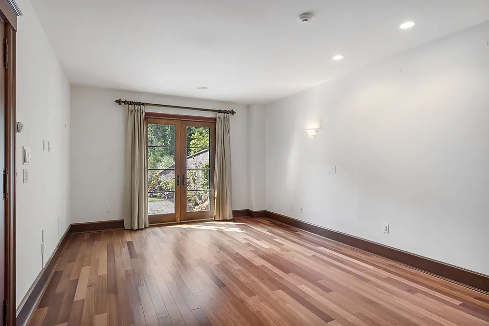 Warm cherry-toned hardwood floor in an empty room with french doors